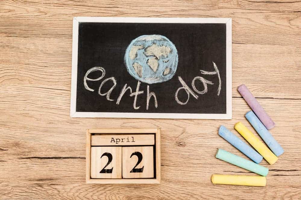 A small slate with a drawing of Earth and "Earth Day" written on it, with wooden blocks saying April 22 underneath and a selection of colored chalk alongside.