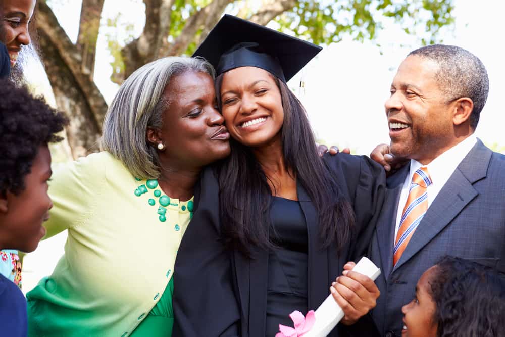 A female African-American college graduate being hugged by her parents.