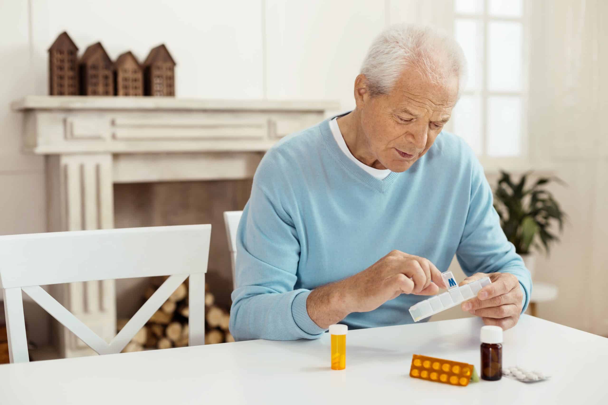 Gray-haired man putting pills in pill case.