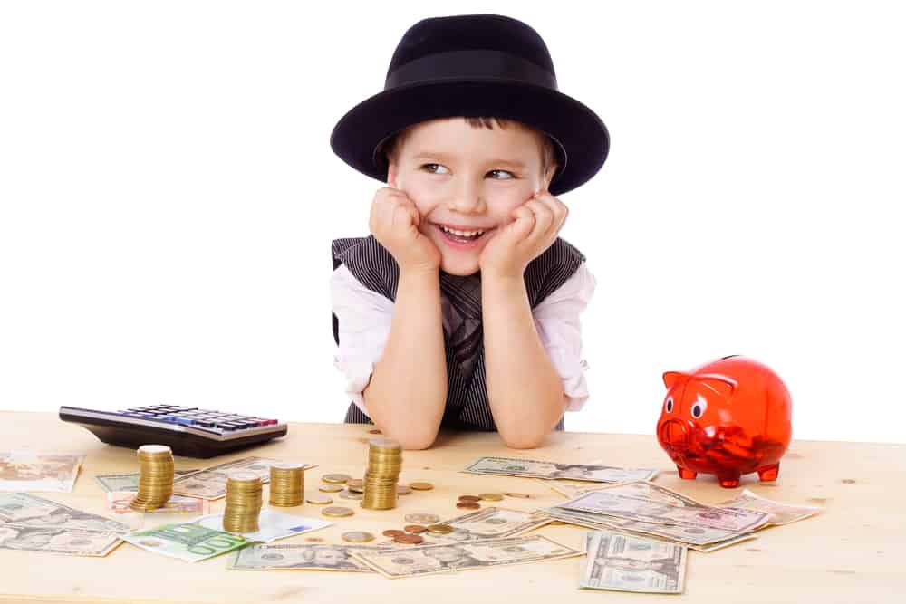 Little boy surrounded by coins, a piggy bank and a calculator.