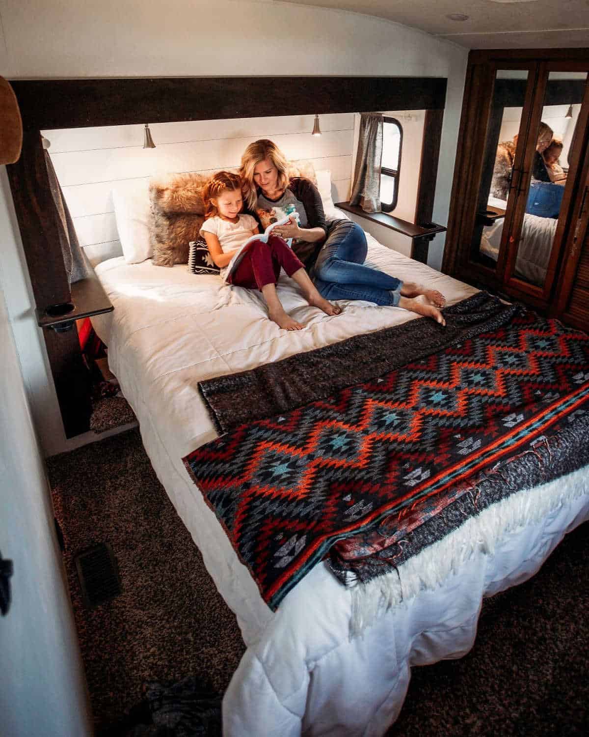 Woman reading to child on large bed in luxury RV while glamping