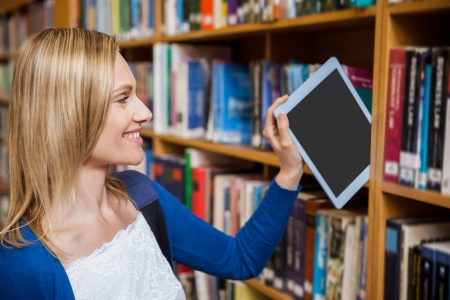 Woman placing tablet on shelf with library books