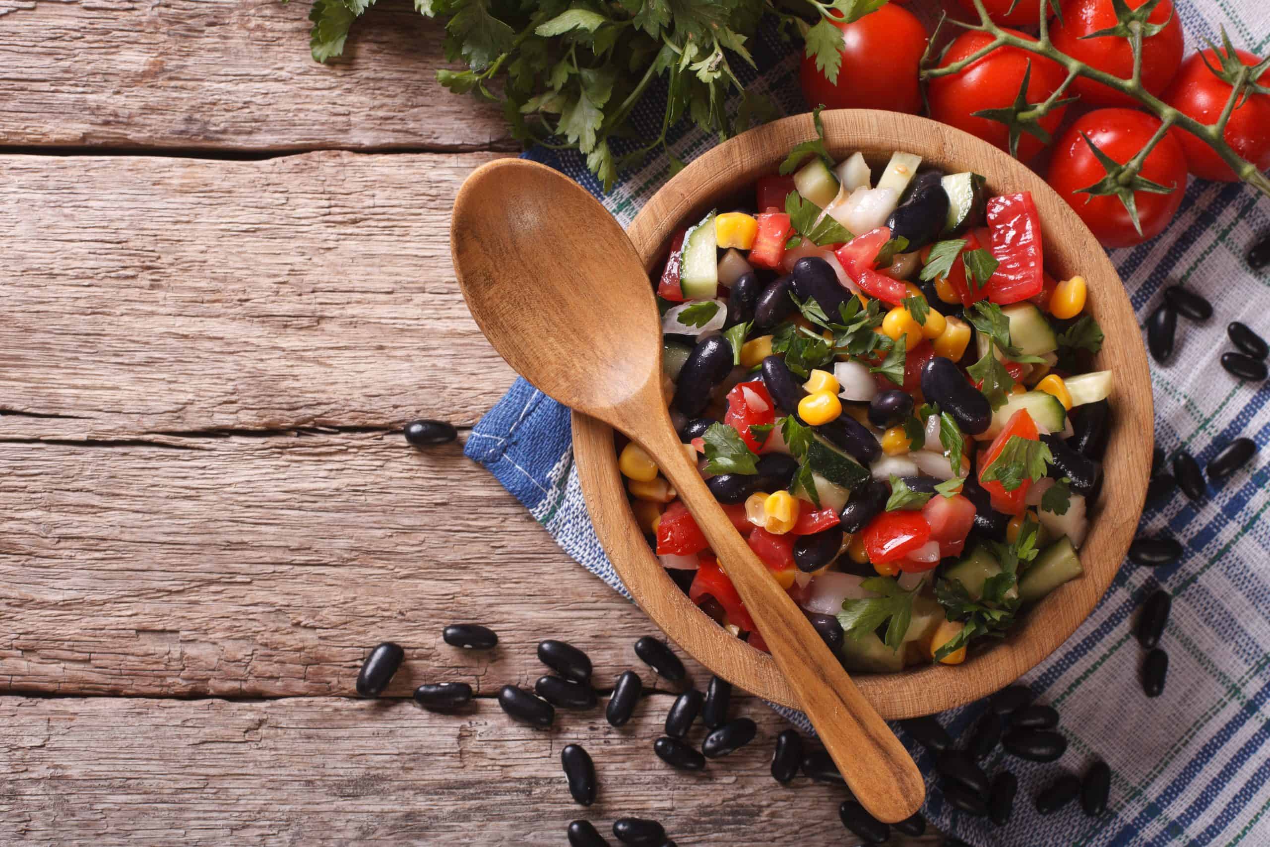 Salad with greens, black beans, corn and tomatoes in a wooden bowl with wooden spoon 