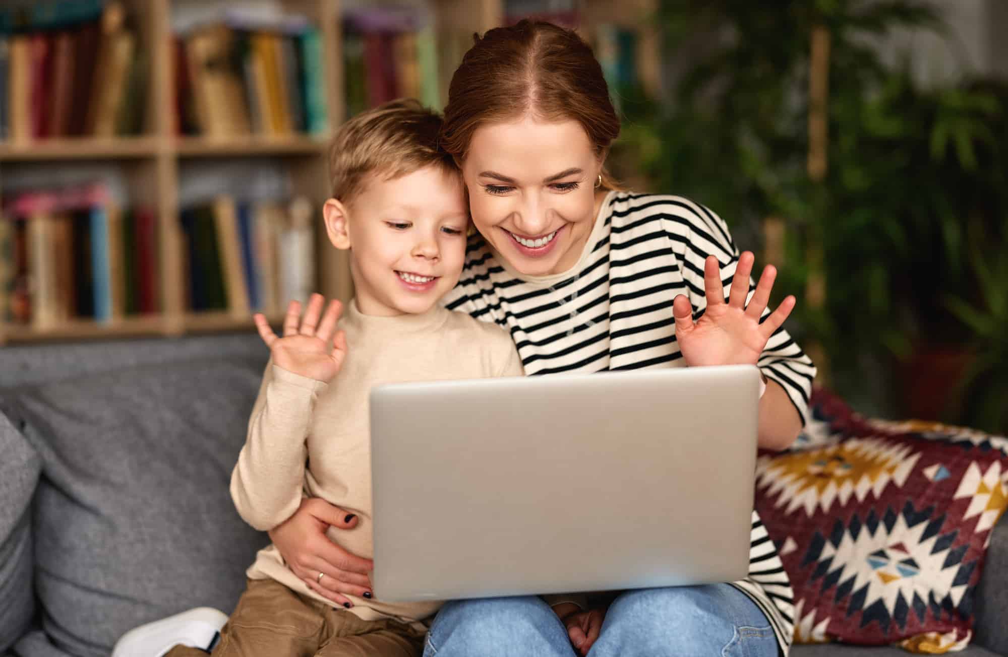 Young mother and son waving to family member on laptop for video call