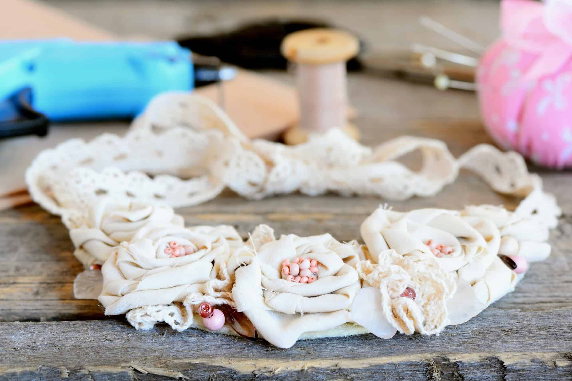 A wreath made from scraps of ivory fabric with pink seed pearl centers and pink thread in backgroud