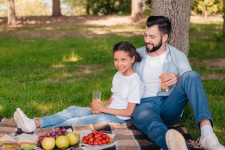 Perfect summer picnic - dad and young girl having a picnic on a blanket with fruit and sandwiches