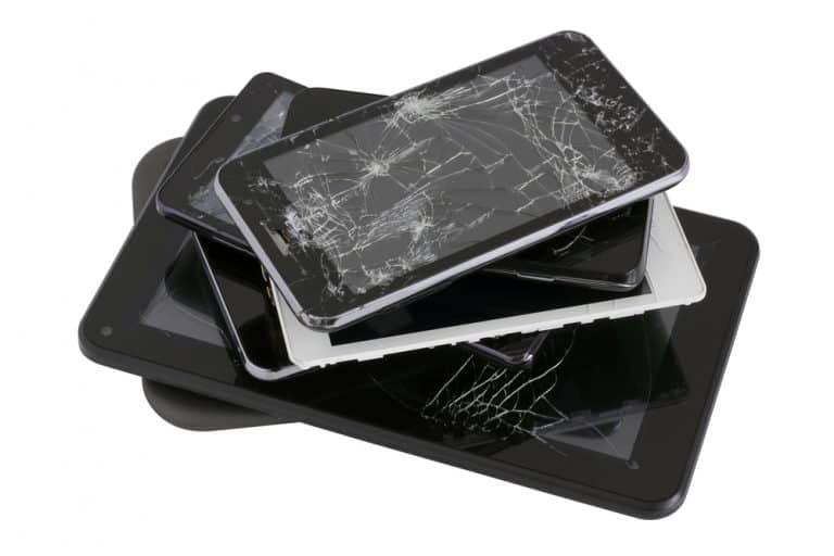 a stack of old cell phones, tablet, with cracked screens