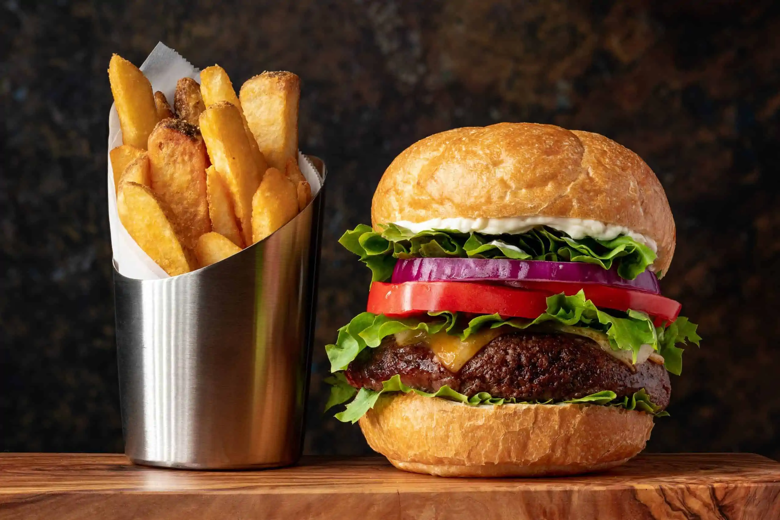 Hamburger day deals - Picture of cheeseburger with lettuce, tomato and red onion next to metal container of thick steak fries