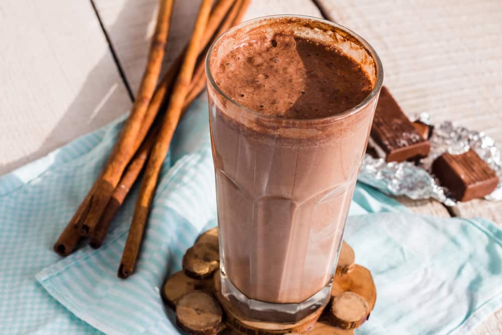 Chocolate smoothie in glass surrounded by cinnamon sticks