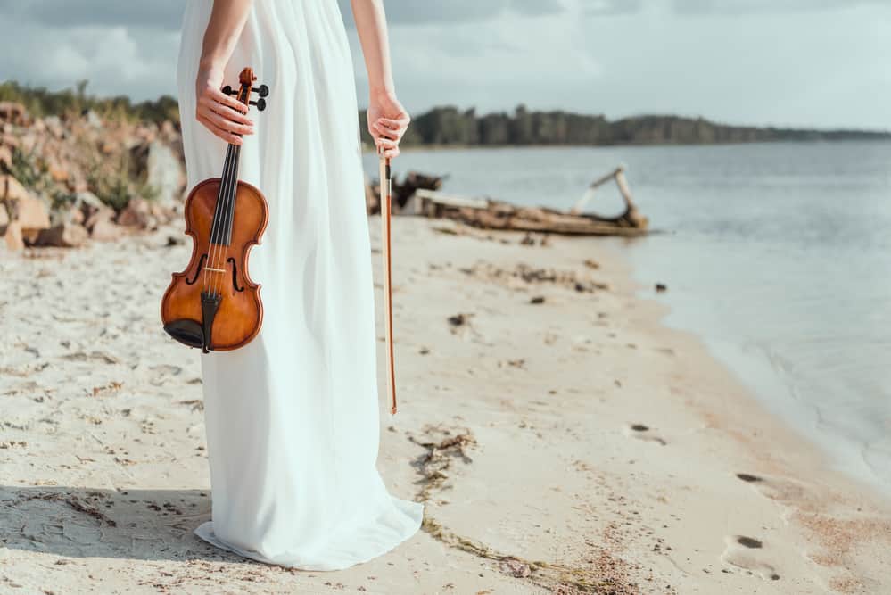 Female violinist in long white dress on beach