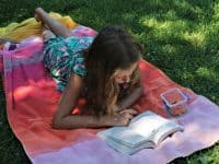 Summer reading programs - girl on striped blanket in grass reading a book