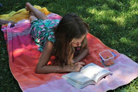 Summer reading programs - girl on striped blanket in grass reading a book