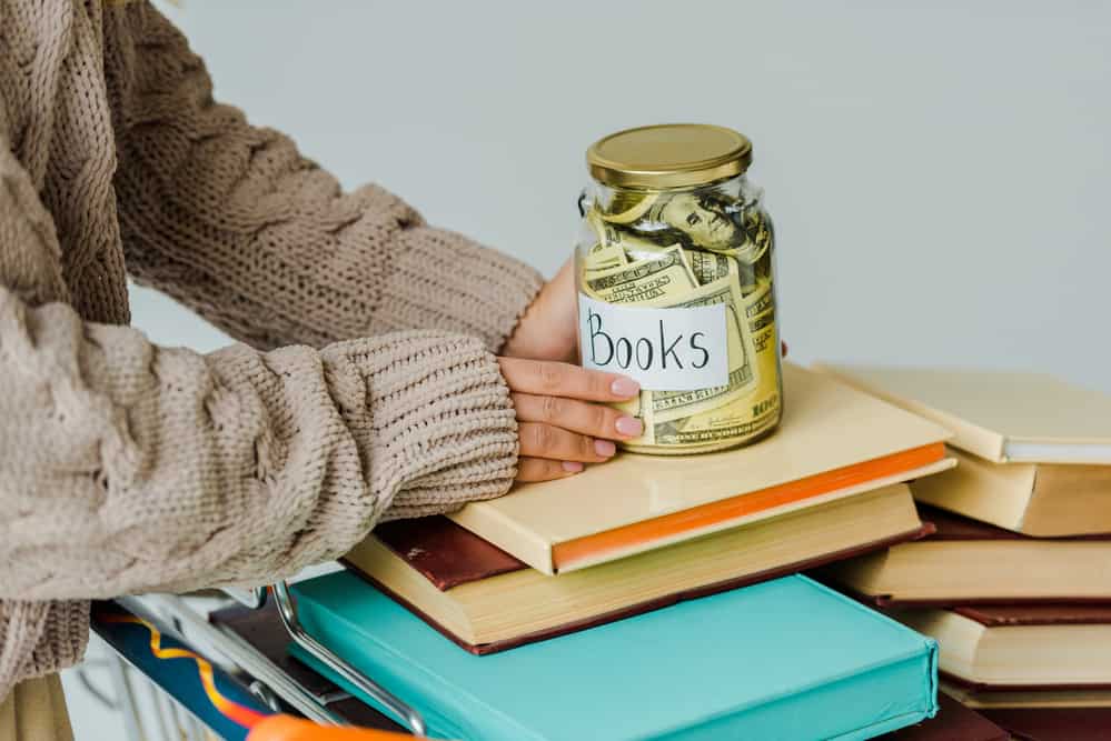 Closeup of a jar labeled "books" full of dollar bills, on top of a stack of books.
