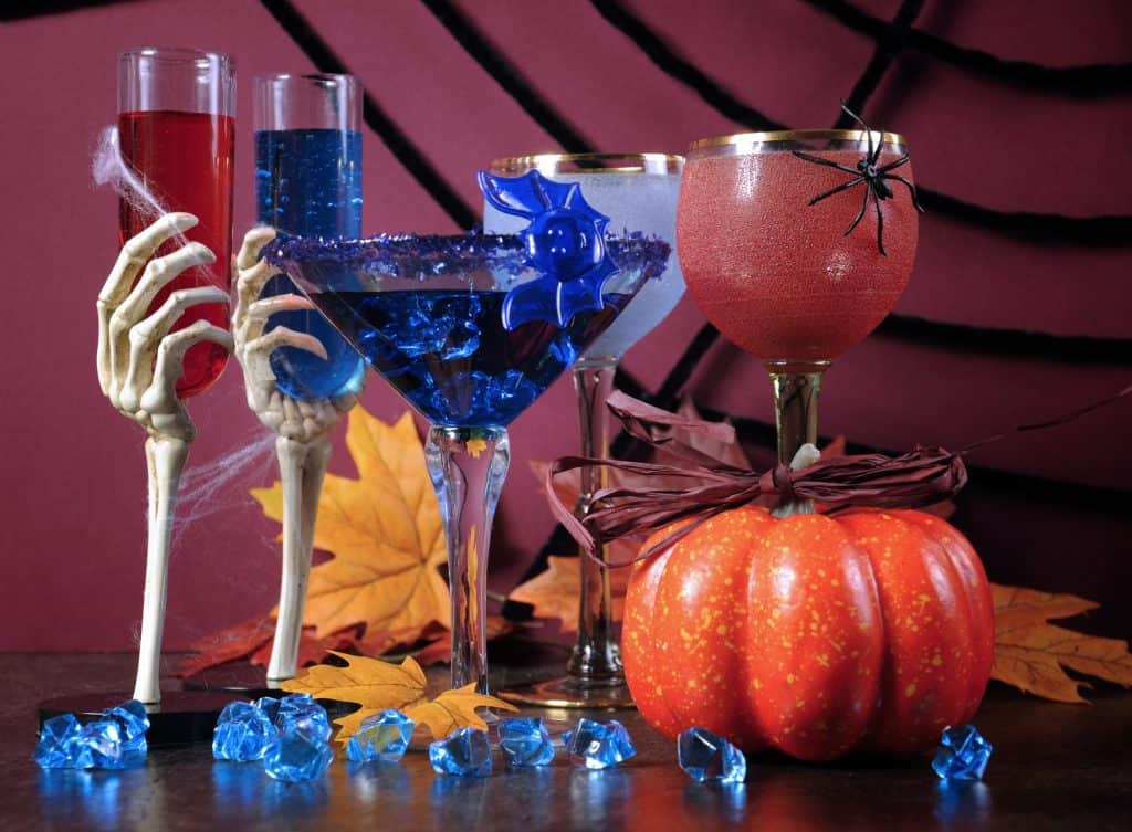 Happy Halloween ghoulish party cocktail drinks with spider web and decorations on purple background.
