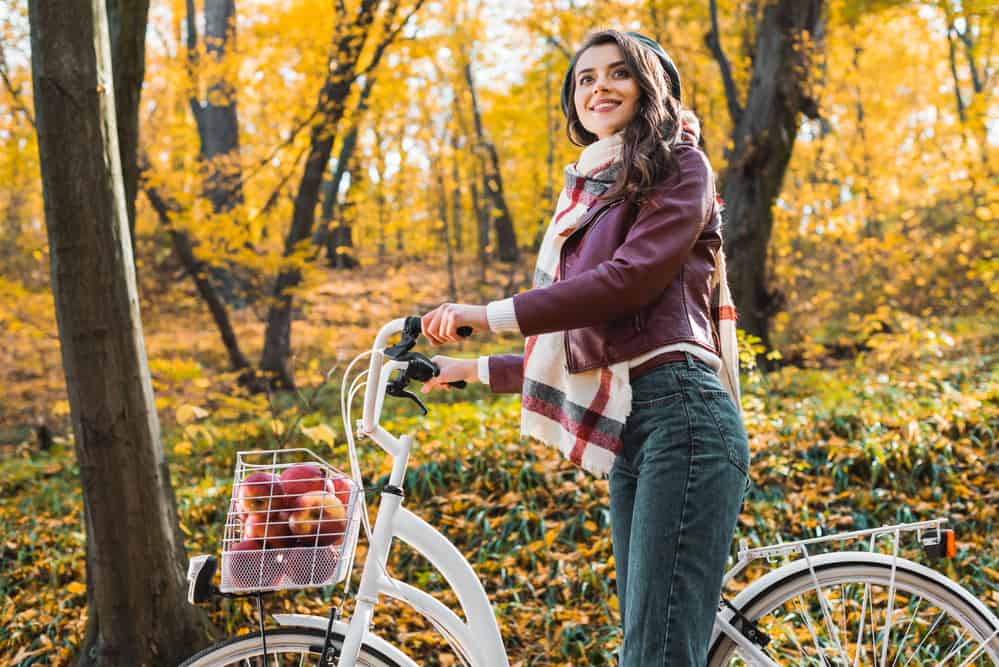 Woman on bike in autumn woods wearing leather jacket with checked scarf and jeans.