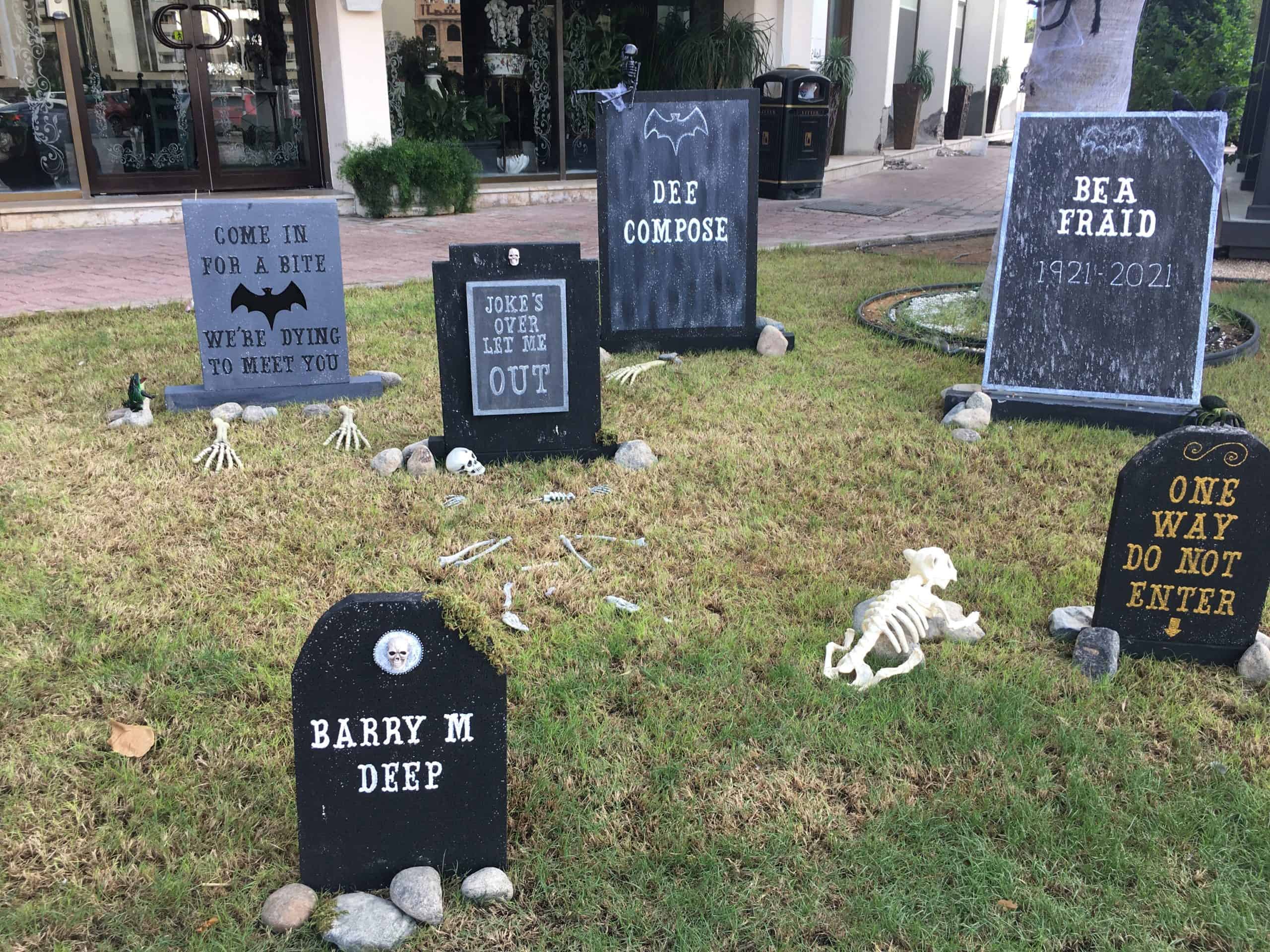 Homemade gravestones in a yard with humorous sayings as a Halloween decoration. 