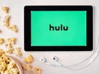Tablet with hulu logo, surrounded by popcorn and earbuds.
