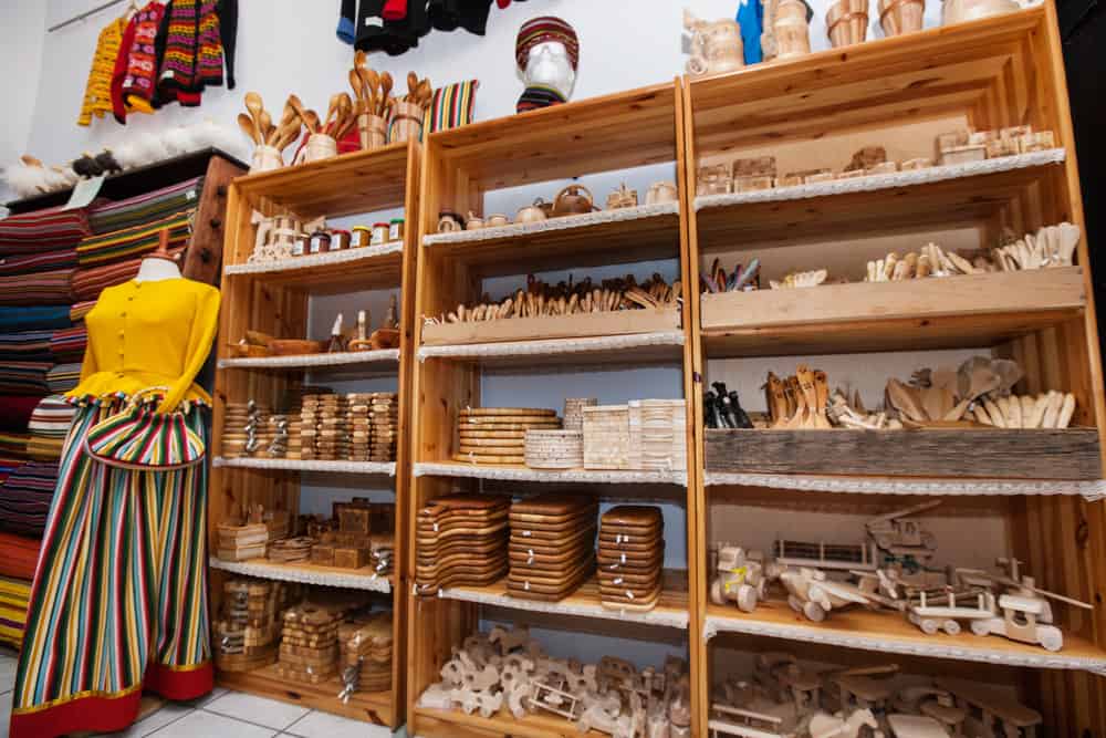 Colorful handmade textiles and wooden handicrafts displayed on shelves in gift shop.