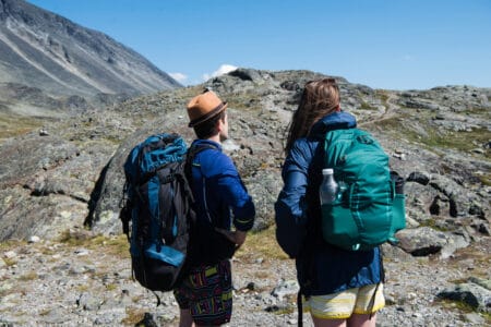 A male and a female hiker shown from the back, looking at mountains in the distance.
