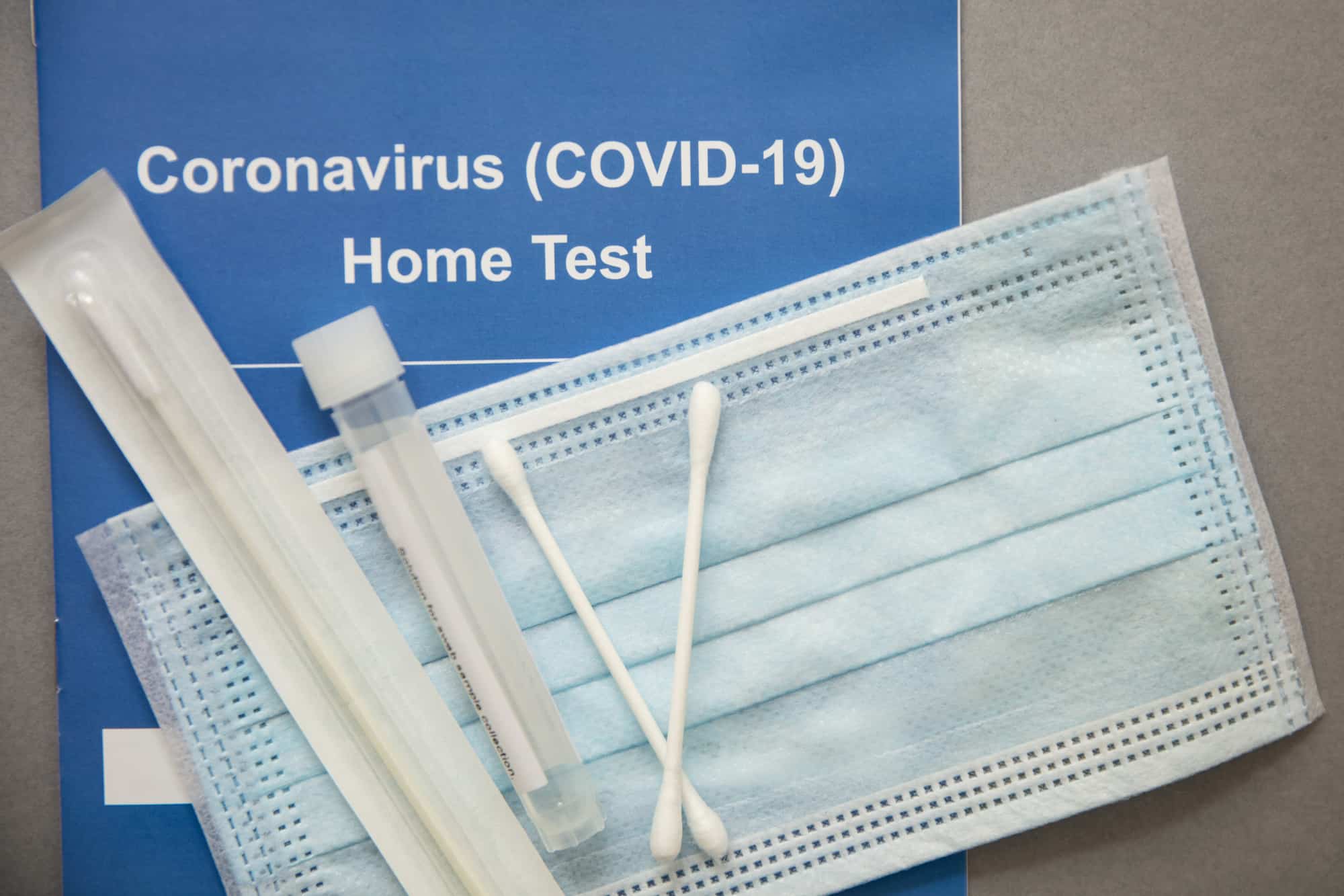 At-home test kit for COVID with swabs, sealed packets and blue mask in background