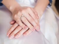 Closeup of woman's hands with diamond engagement ring clasped on her white bridal gown
