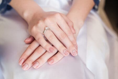 Closeup of woman's hands with diamond engagement ring clasped on her white bridal gown