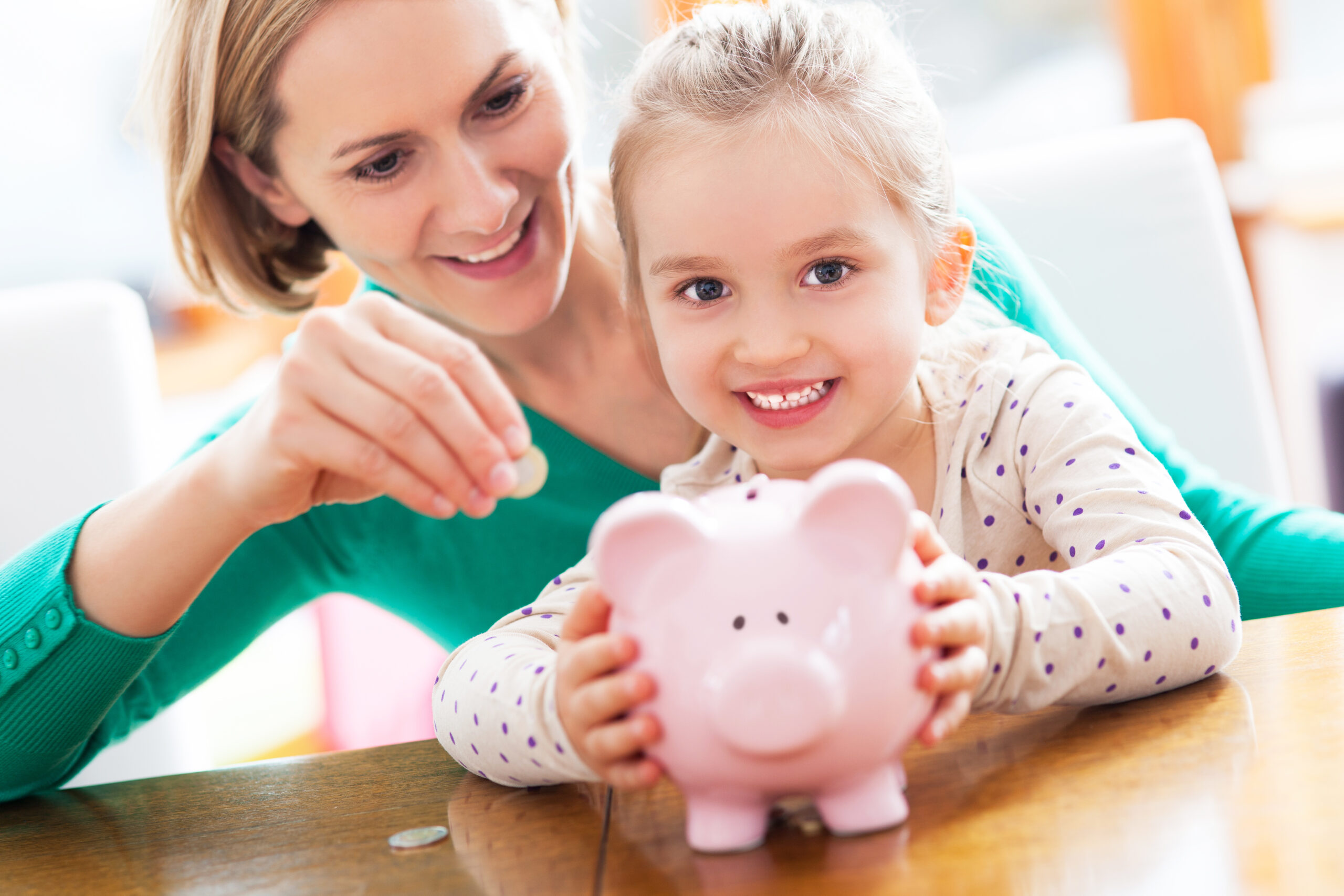A mother helping her young daughter put coins in a piggy bank.
