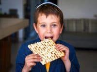 Boy with brown hair and blue eyes wearing yarmulke and eating matzo at Passover