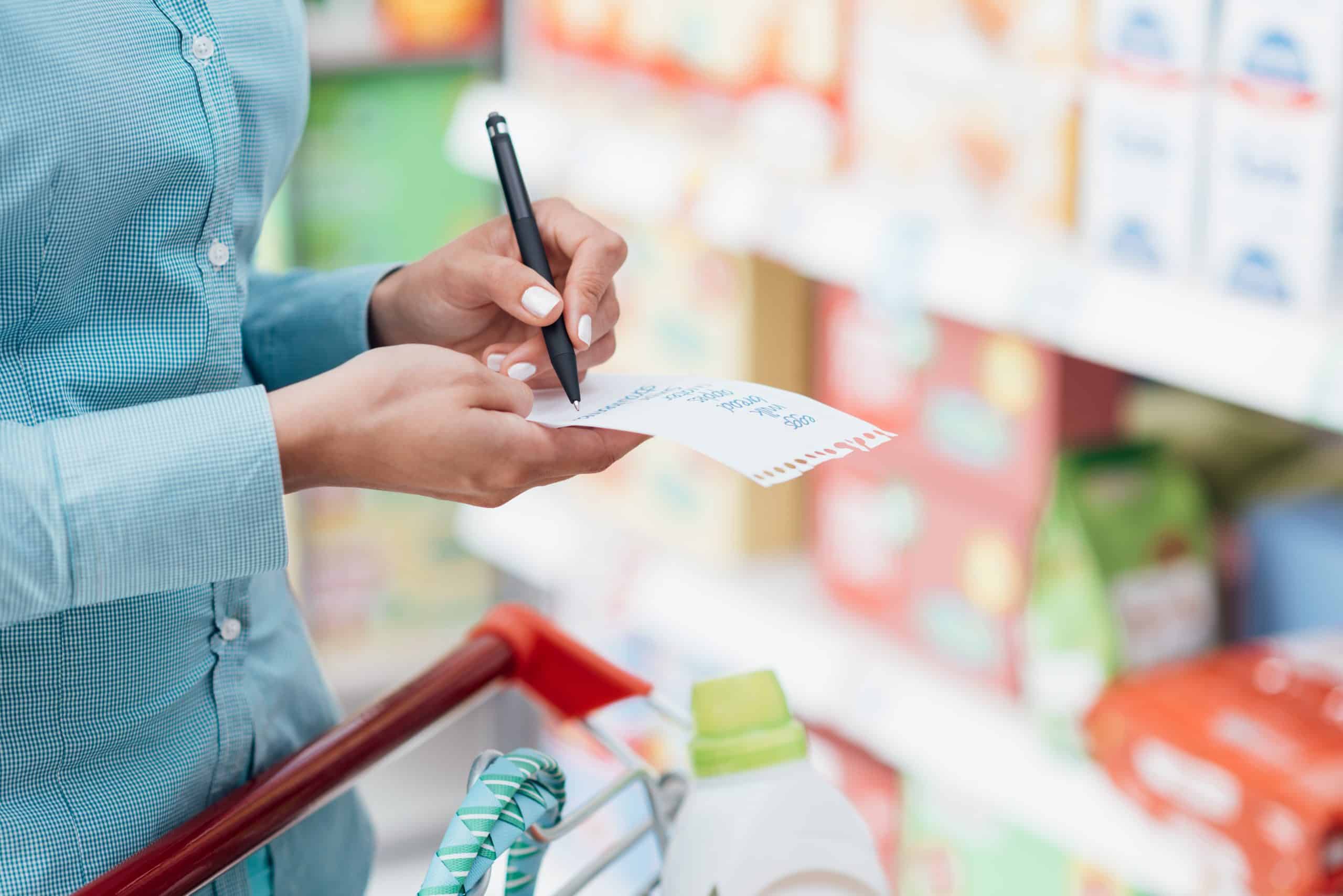 Closeup of woman's hand crossing off items on list in grocery store