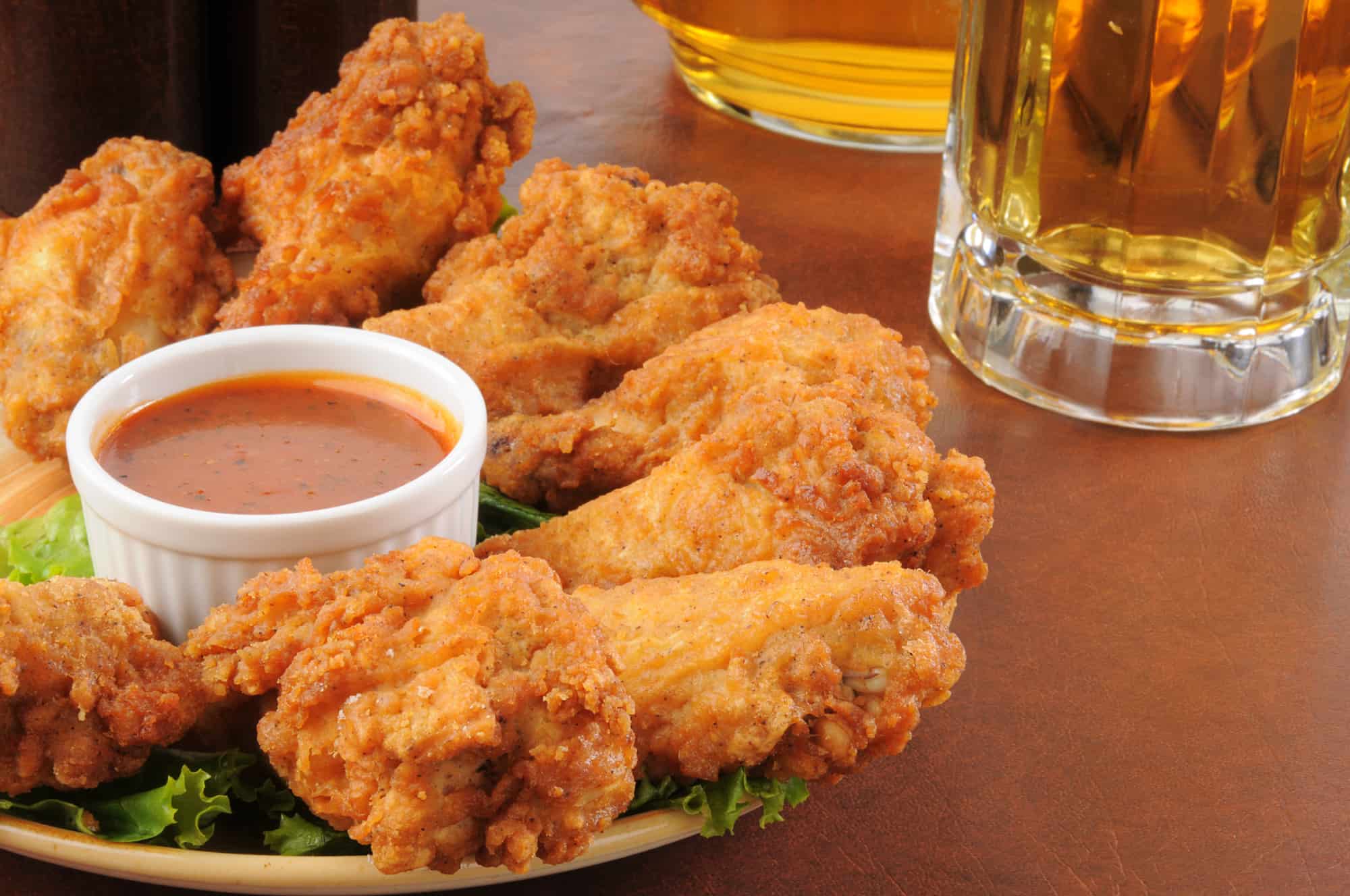 Chicken wings on a plate around a container of sauce with mug of beer in background