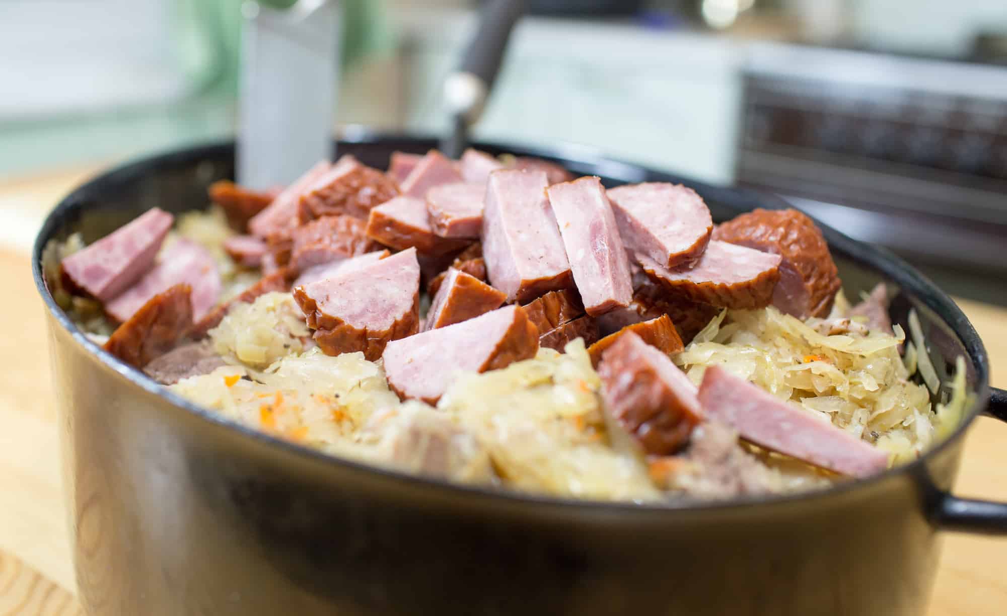 Closeup of slow cooker with sauerkraut and slices of sausage on top.