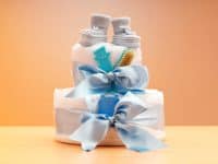 A two-tier cake made of stacked diapers tied with a blue ribbon with baby booties on top. baby