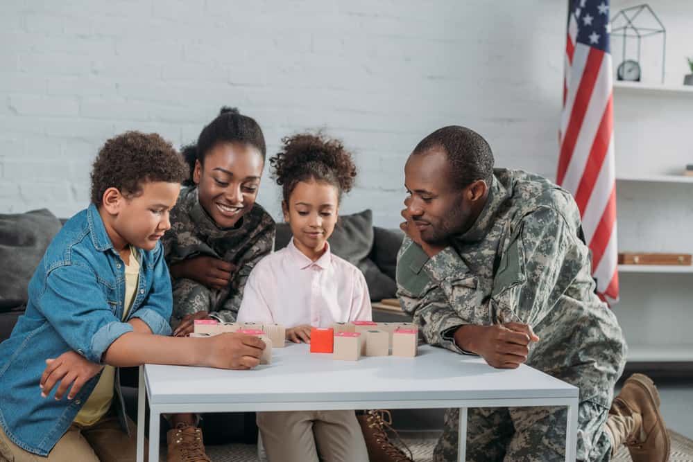 A man and woman in military uniform play a board game with a boy and girl.