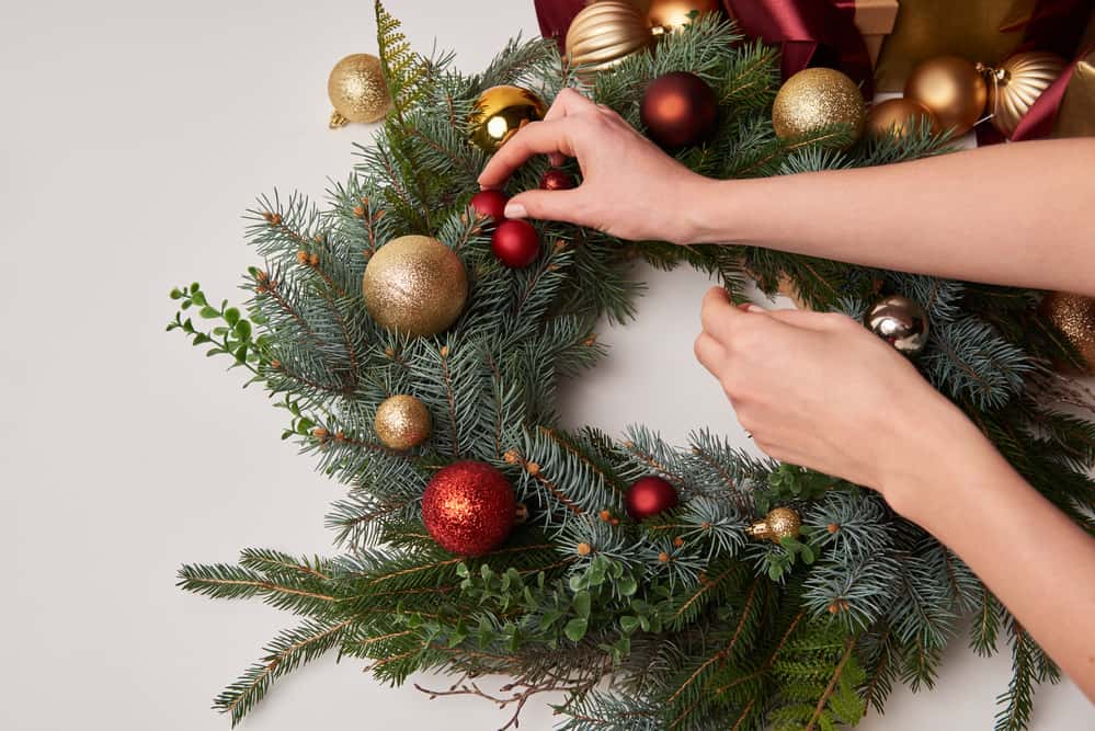 A woman's hands placing ornaments on a pine wreath.