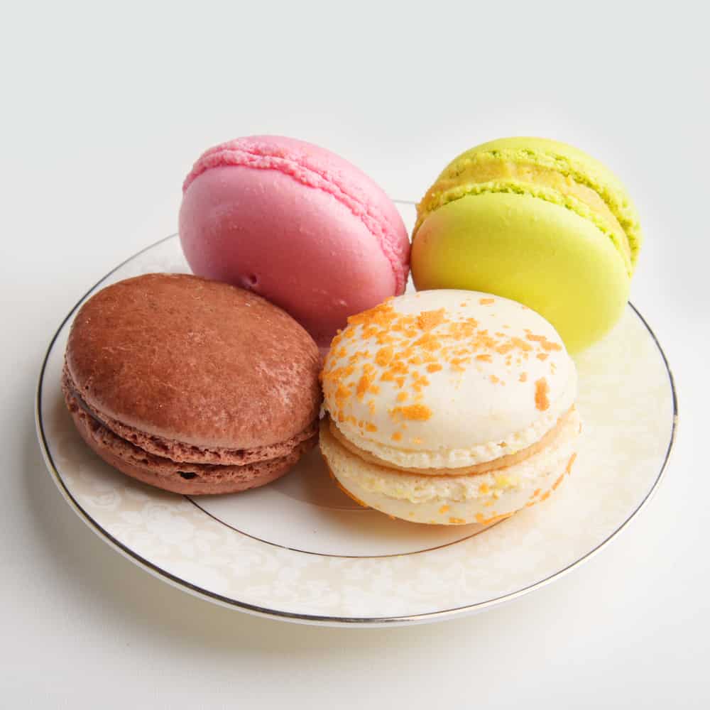 Four pastel-colored macarons on a small white plate.