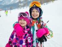 2 young girls in ski gear embrace on a ski slope