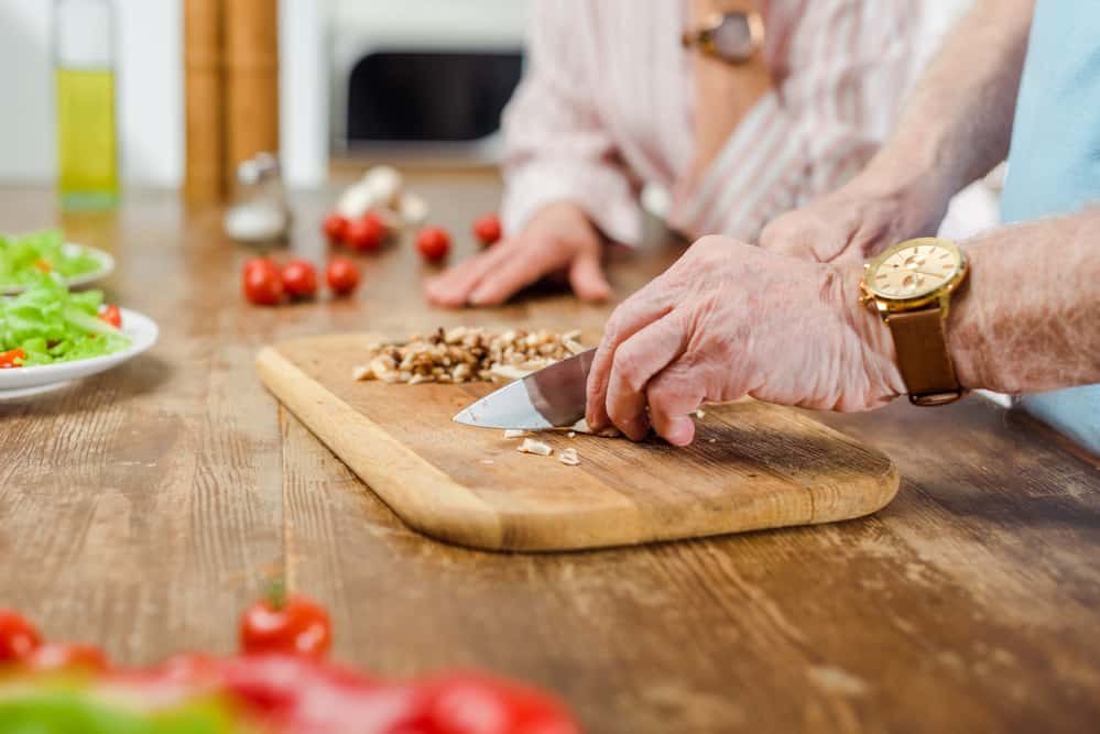 Closeup of older man chopping ingredients on a cutting board