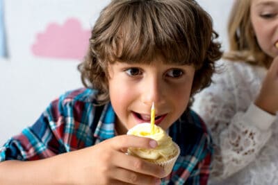 Boy eating cupcake with candle at birthday party;