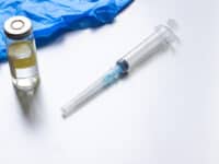 A syringe, blue medical gloves and a vial of vaccine.