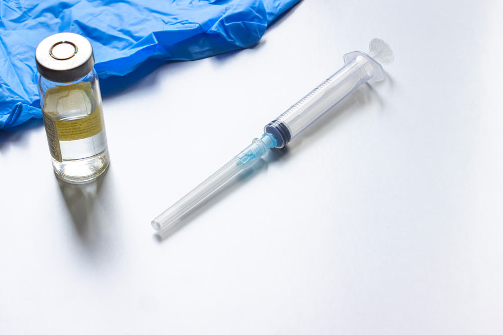 A syringe, blue medical gloves and a vial of vaccine.