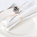 An all-white place setting with white plate and white napkin on white tablecloth, with a silver pine cone.