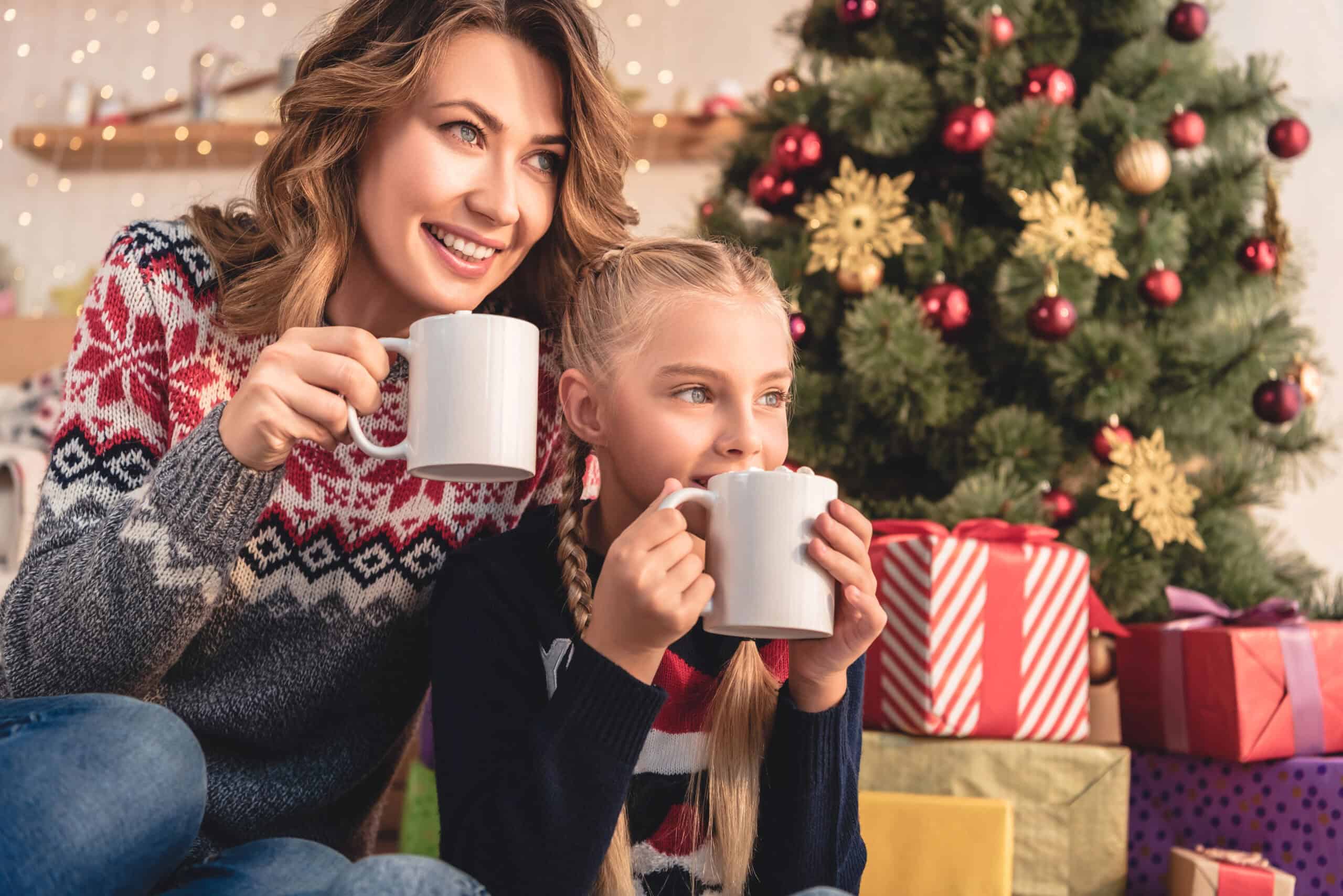 two girls drinking hot cocoa by the Christmas tree