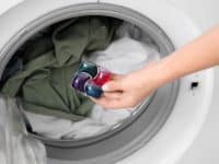 Young woman putting laundry detergent into washing machine, closeup