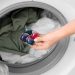 Young woman putting laundry detergent into washing machine, closeup