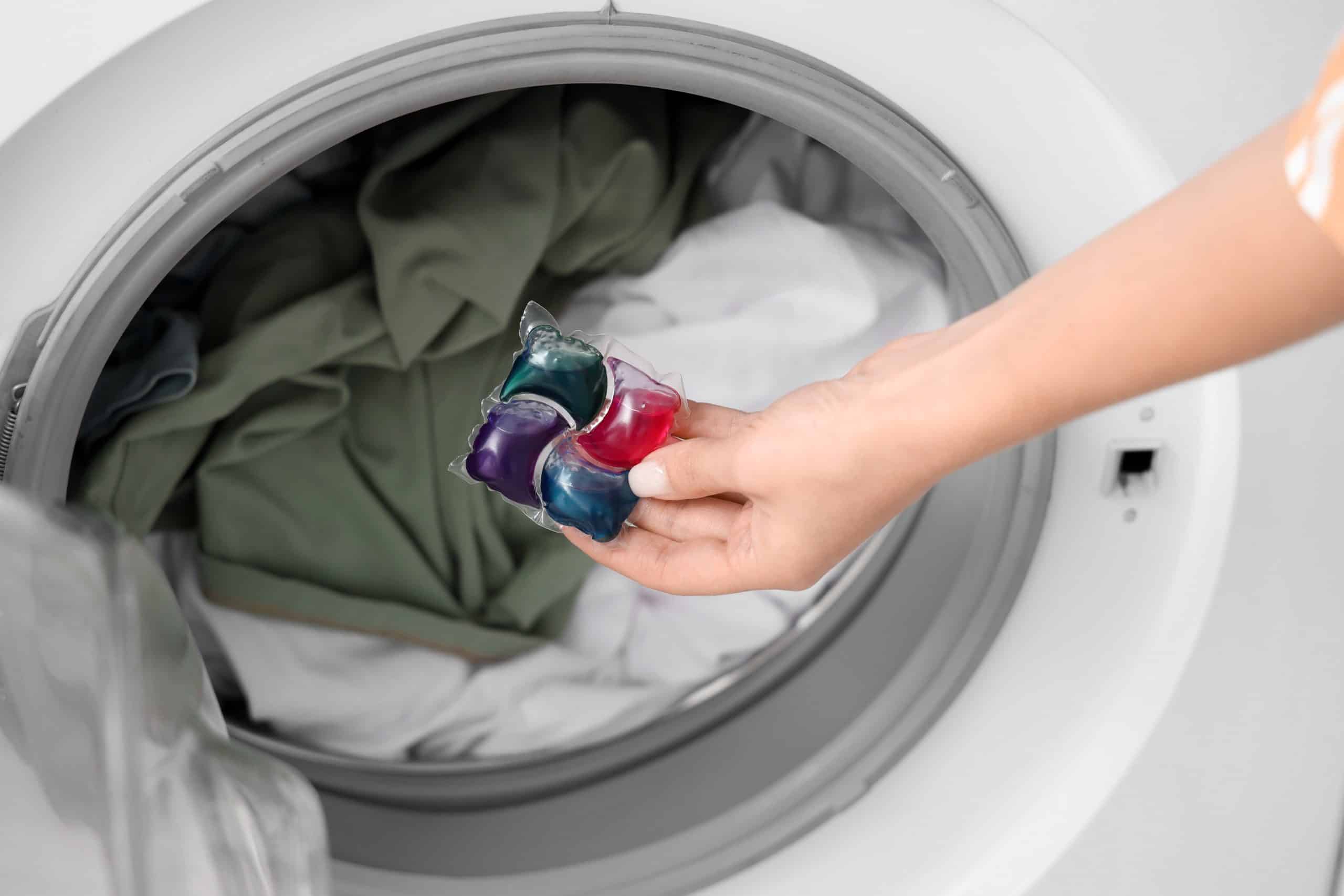 Young woman putting laundry detergent into washing machine, closeup